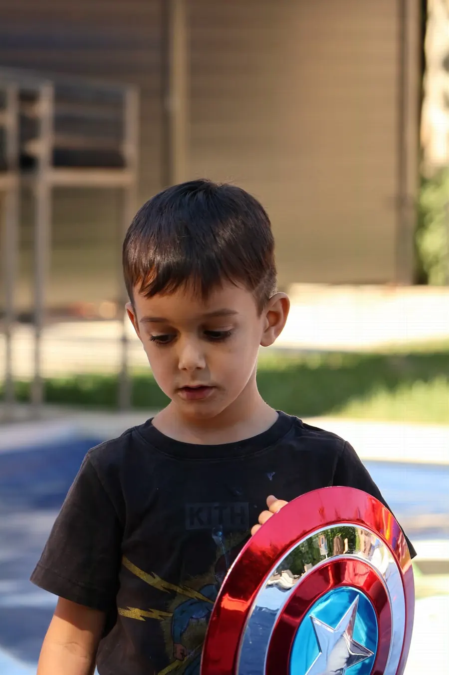 Young boy holding a Captain America shield outdoors at a party, photographed by Lihi Matzri